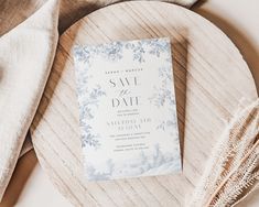 a white and blue wedding save the date card on a wooden platter next to some napkins