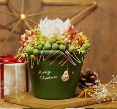 a green pot filled with lots of flowers on top of a wooden table next to presents