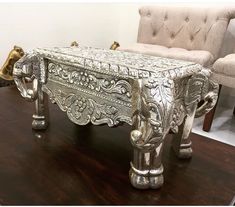 an ornate silver bench sitting on top of a wooden table next to a chair and ottoman