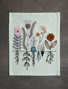 an embroidered wall hanging with flowers and leaves on white linen, against a gray background