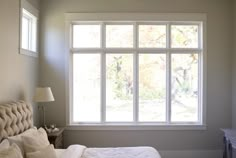 a woman standing in front of a large window next to a bed with white sheets