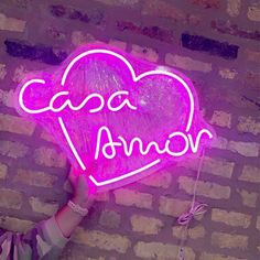 a person holding up a neon sign that says cocoa annor on the side of a brick wall