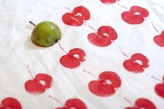 a green apple sitting on top of a white tablecloth covered in red cherries