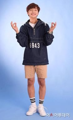 a young man standing in front of a blue background wearing shorts and a hoodie