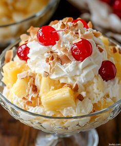 a dessert dish with pineapples, cherries and whipped cream in a glass bowl