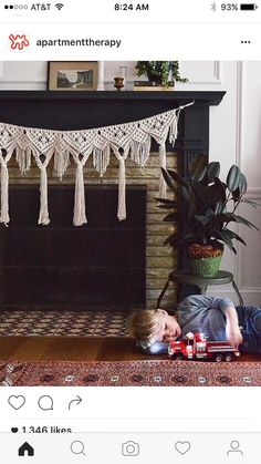 a little boy laying on the floor next to a fire place with a toy train in front of him