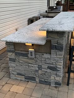 an outdoor bar made out of stone with lights on it's sides and chairs around it