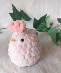 a small stuffed animal sitting on top of a white fur covered floor next to green leaves