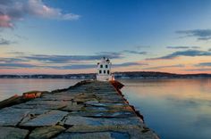 a lighthouse sitting on top of a stone pier next to the ocean under a cloudy blue sky