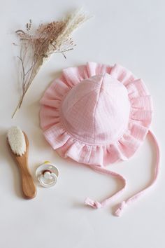 a pink hat and brush on a white surface next to some dried flowers, cotton swab