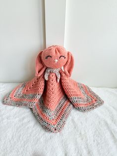 a crocheted pink stuffed animal sitting on top of a white bed next to a wall