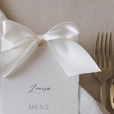 a table setting with silverware and a white menu card tied to a satin ribbon