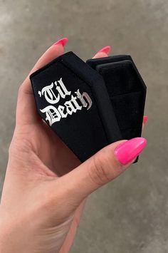 a hand holding a black ring with white writing on it and pink nail polishes