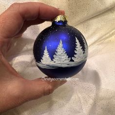 a hand holding a blue ornament with white trees on it