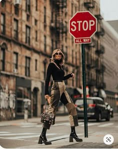 a woman crossing the street in front of a stop sign and all way sign with her handbag