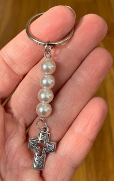 a person is holding a key chain with a cross on it and pearls hanging from the end