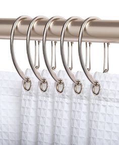 four metal hooks hang on the side of a white curtain with silver rings attached to it