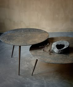 two round tables sitting on top of each other in front of a wall with a vase