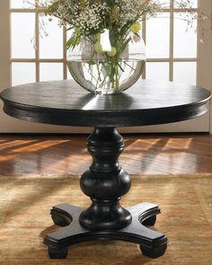 a vase with flowers on top of a table in front of an open window and rug