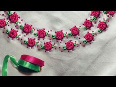 a necklace with pink roses on it and a green ribbon next to the bead