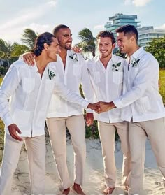 three men in white shirts and tan pants are standing on the beach with their arms around each other