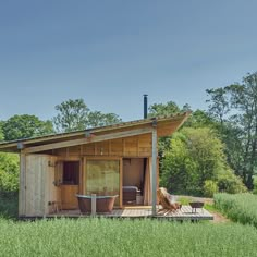 a small wooden cabin in the middle of a grassy field with a hot tub and patio