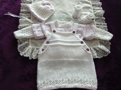 three knitted baby clothes laid out on a purple blanket