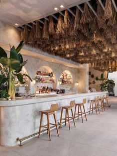 the bar is decorated with plants and hanging lights above it, along with wooden stools