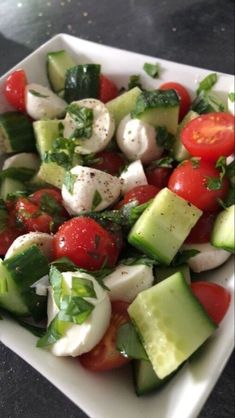 a square white plate filled with cucumber, tomato and mozzarella salad