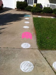 the sidewalk has pink and white dots painted on it, along with green grass in front of a house