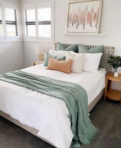 a bed with white sheets and green blankets in a bedroom next to two nightstands