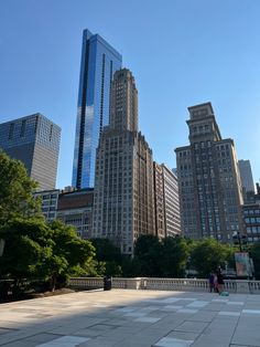 people are walking around in the city with tall buildings behind them and one person is sitting on a bench