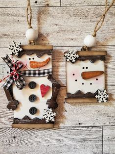 two snowmen are hanging from wooden boards on the wall, one is decorated with buttons and ribbon