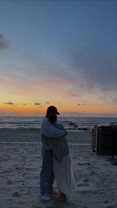 a man and woman hug on the beach at sunset