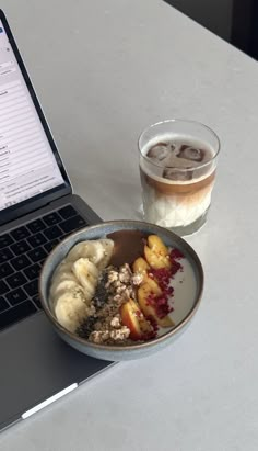 an open laptop computer sitting on top of a white table next to a bowl of food