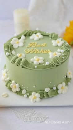 there is a green cake with white flowers on the top and gold writing on the bottom