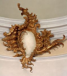 an ornate gold mirror hanging from the ceiling in a room with white walls and trimmings