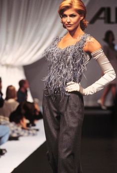 a woman is walking down the runway in a feathered top and wide legged pants