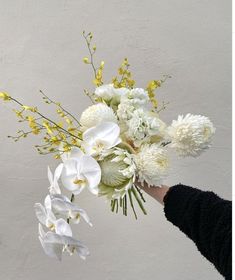 a person holding a bouquet of flowers in front of a white wall with yellow accents