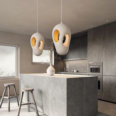 two lights hanging from the ceiling above a kitchen island with stools in front of it