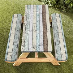 an outdoor picnic table made out of wood and cement tiles on the grass in front of some bushes