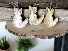 three metal cats are hanging on a wooden shelf next to a potted green plant