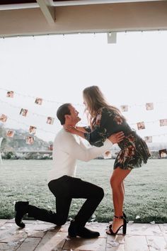 a man kneeling down next to a woman on top of a stone floor in front of a grass field