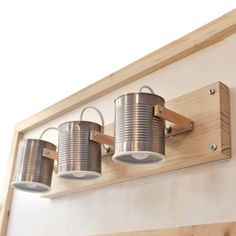 three metal buckets mounted on a wooden shelf above a light fixture in a room