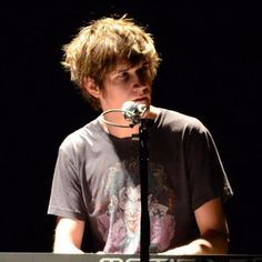 a young man standing at a keyboard in front of a microphone with his head turned to the side