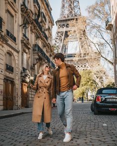 a man and woman walking down the street in front of the eiffel tower