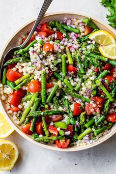 a bowl filled with asparagus, tomatoes and other vegetables next to lemon wedges