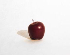 an apple sitting on top of a white surface next to a shadow in the floor