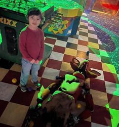 a young boy standing next to a fake dinosaur in a room with green and red checkered floors