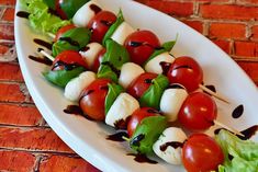 a white plate topped with skewered tomatoes and mozzarella on top of lettuce